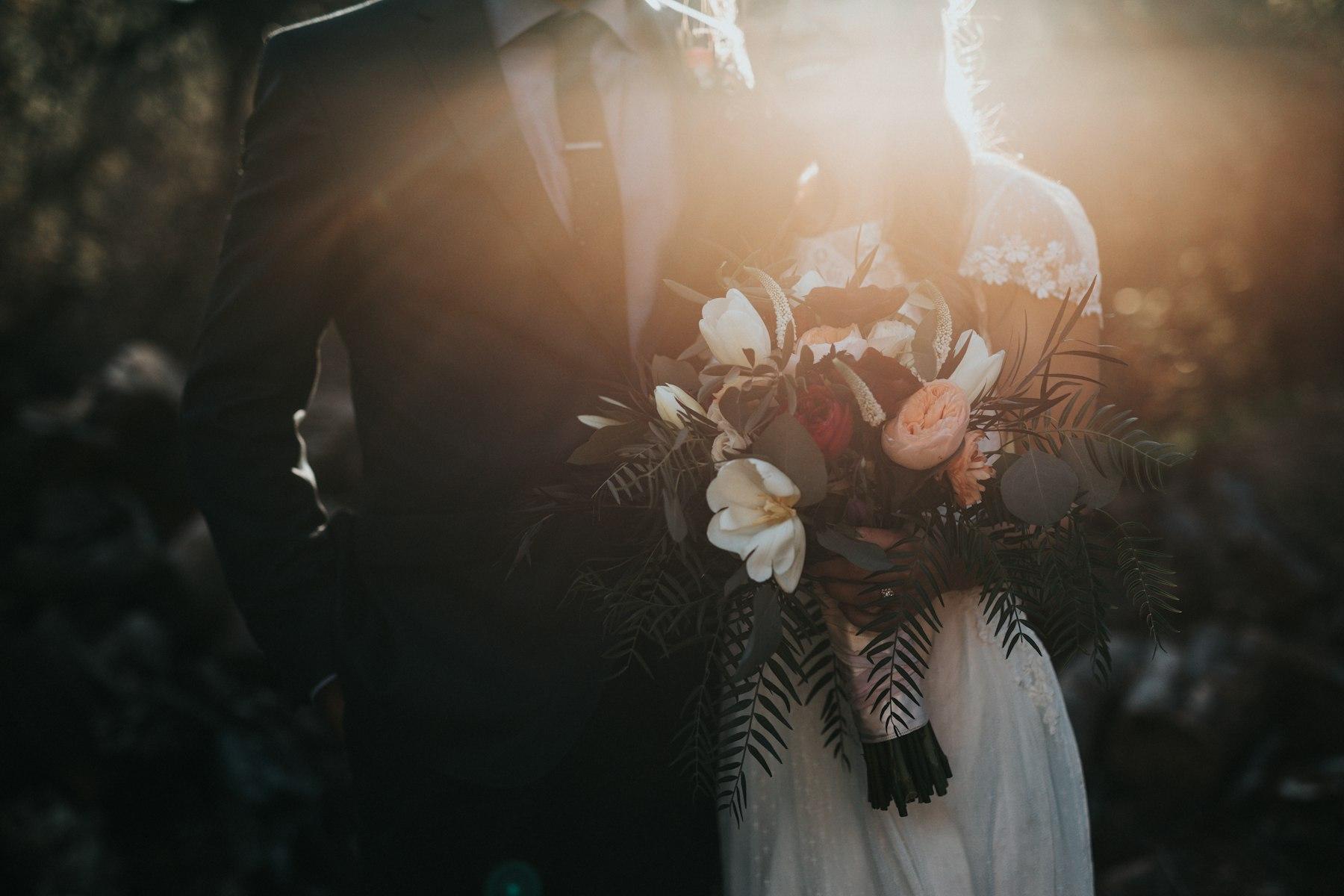 A wedding couple in warm light, the bridal bouquet held between them
