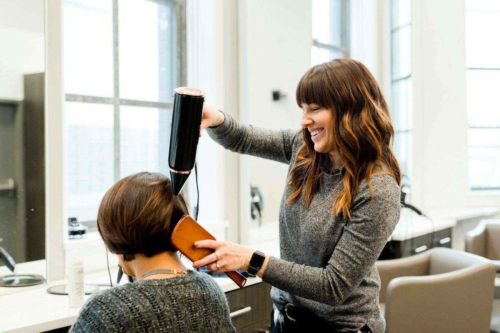A stylist blow-drying a client’s hair in a bright salon