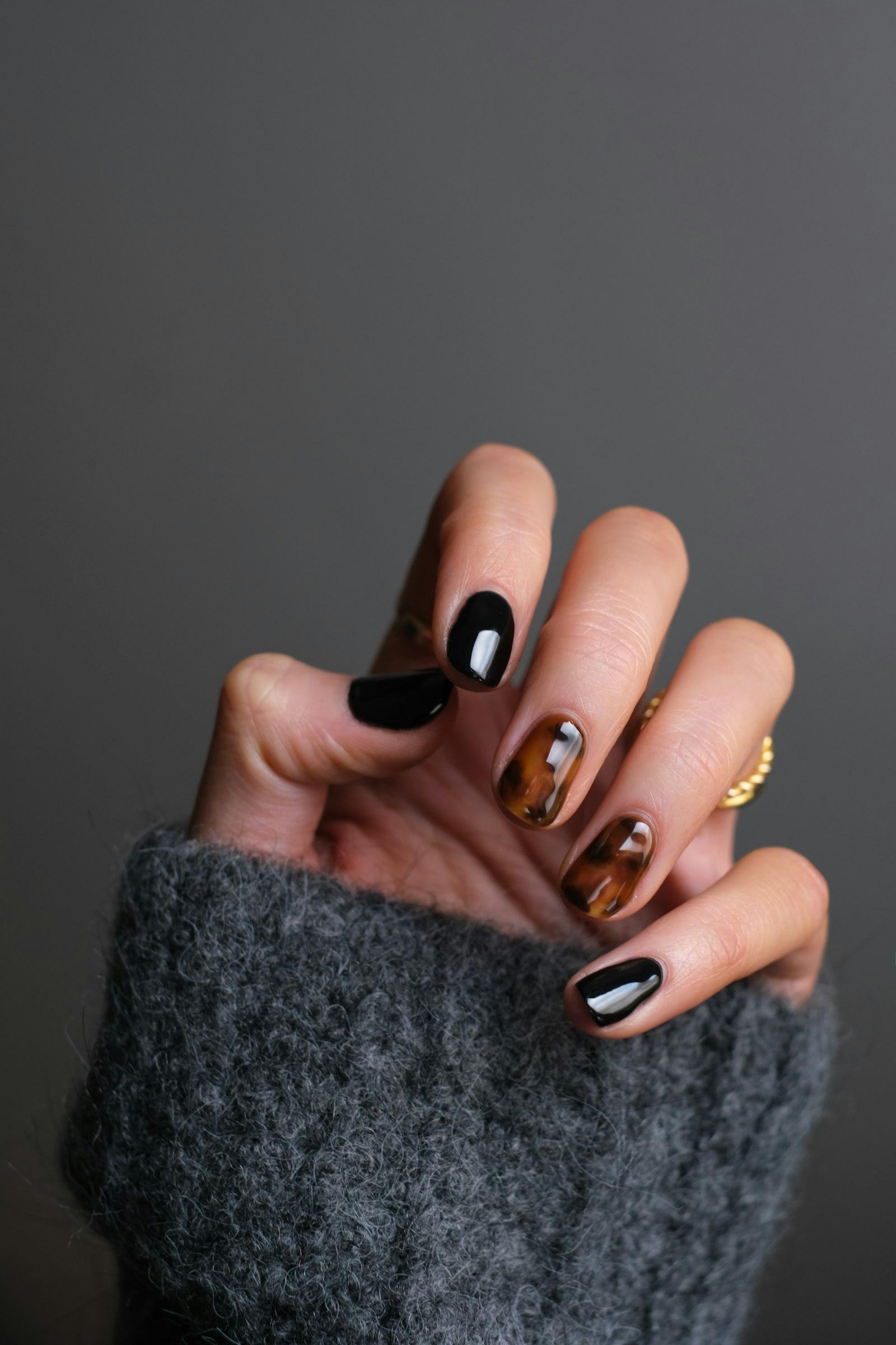A manicure in black and tortoiseshell, with a gold ring